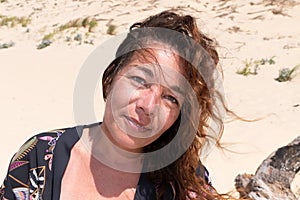 Pretty middle aged woman curly hairs in wind in sand beach summer vacation