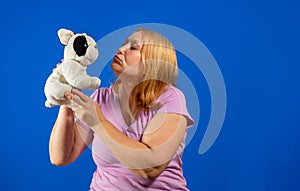 Pretty middle aged woman giving a kiss to a stuffed puppy isolated on blue studio background