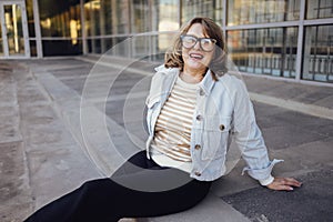 Pretty middle-aged woman in glasses sits on the steps outdoors