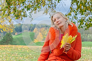 Pretty middle-aged woman holding autumn maple leaves outside in colorful fall nature background