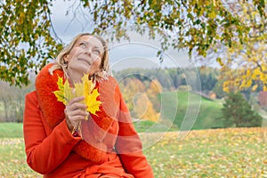 Pretty middle-aged woman holding autumn maple leaves outside in colorful fall nature background with copy space