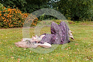 Pretty middle aged woman is laughing lying down on a lawn in a park