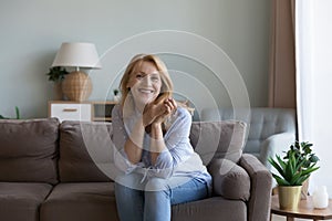 Pretty middle-aged woman posing for picture seated on sofa