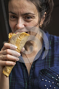 A pretty middle-aged woman in a purple plaid shirt is eating a pizza cone. Fast food. Delicious pizza