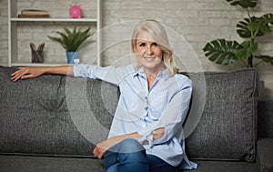 Pretty middle aged woman is sitting on a sofa at home