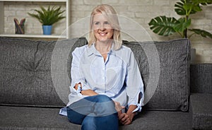 Pretty middle aged woman is sitting on a sofa
