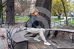 Pretty middle-aged woman of a sports type in a jacket and sweatpants sits in a park on a bench, spring landscape