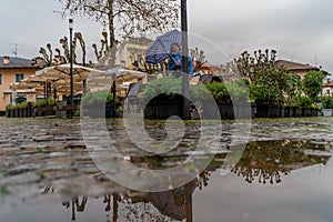 Pretty middle aged woman standing in the rain with an umbrella in a small square in Stresa