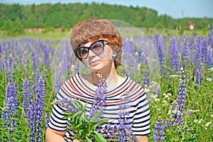 A pretty middle-aged woman in sunglasses stands among flowering lupins