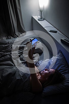 Pretty, middle-aged woman using her cell phone in bed at night