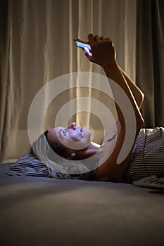 Pretty, middle-aged woman using her phone before sleep in bed