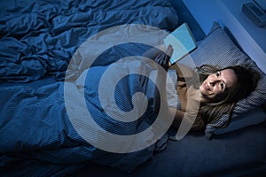 Pretty, middle-aged woman using her tablet computer before sleep