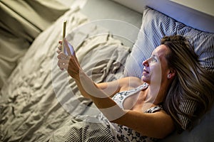 Pretty, middle-aged woman using her tablet computer before sleep in bed