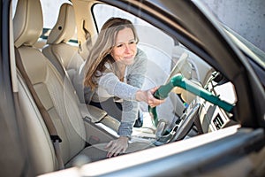 Pretty, middle aged woman vacuum cleaning the interior of a  car