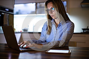 Pretty, middle-aged woman working late in the day on a laptop computer at home,