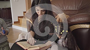 Pretty Middle Eastern woman reading the book to little children. Mother educating her lovely son and daughter at home.