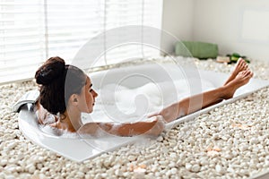 Pretty millennial woman lying in bathtub with foam, enjoying bubble bath in morning at hotel, copy space