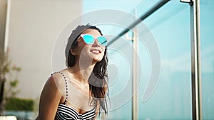 Pretty mixed race woman in sunglasses and bikini posing in swimming pool. Gorgeous lady enjoying her summer vacation at