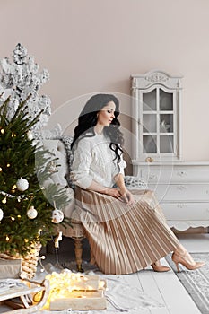 Pretty model girl with dark hair wearing skirt and white sweater in the interior decorated for Christmas