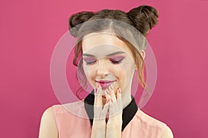 Pretty model woman with fashion makeup, trendy manicure nails and topknot haircut on bright pink background