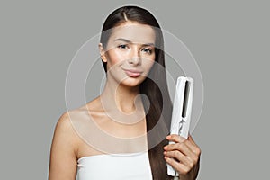 Pretty model woman holding hair iron and straightening her healthy long dark hair on white background. Haircare and hair styling