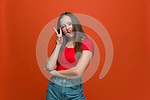 Pretty modern cheeky young girl make v-sign peace gesture winking, showing tongue posing on orange studio background