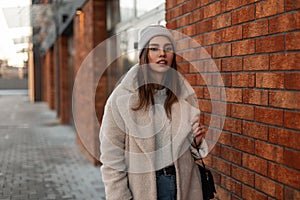 Pretty modern girl with sexy lips outdoors. Fashion model of a young woman in fashionable coat in a knitted stylish hat with a