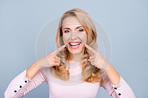 Pretty, modern woman in casual outfit pointing with two forefingers to her beaming healthy smile over grey background photo