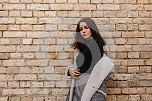 Pretty modern young woman in stylish vintage clothes in retro style posing outdoors in the city near the brick wall