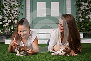 Pretty mom and cheerful daughter playing with two husky puppies on the grass