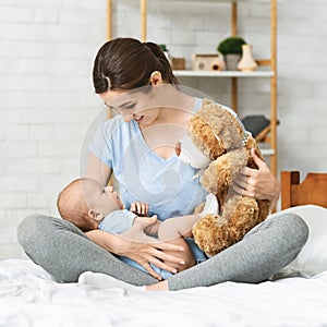 Pretty mom showing soft teddy bear to her newborn baby