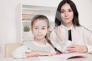 Pretty mother with cute daughter sitting with book in the room at home.