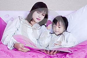 Pretty mother and girl read book on bed