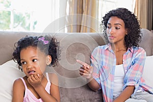 Pretty mother sitting on couch scolding petulant daughter