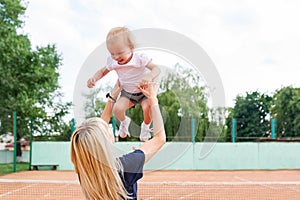 Pretty mum laughing and raising her baby girl with tennis in the background