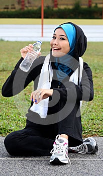 A pretty muslim woman athlete resting while drink