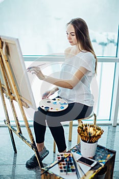 Woman artist painting a picture in a well-lit studio