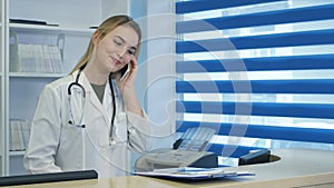 Pretty nurse using tablet and phone at hospital reception desk