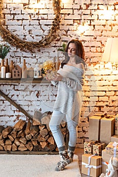 Pretty pacified young woman looking at a gift box standing near a woodpile in a retro decorated vintage New Year`s room photo