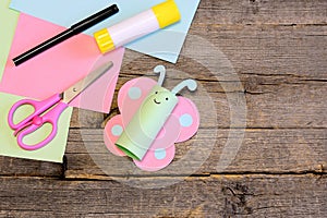 Pretty paper butterfly, scissors, marker, glue stick, colorful paper sheets on a wooden table. Creative paper crafts for children