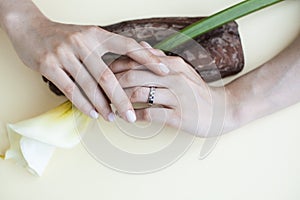 Pretty perfect woman hands with white manicure and big flower on colorful yellow background, spa concept