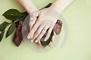 Pretty perfect woman hands with white manicure and green leaf on colorful background with wood, spa cosmetic concept