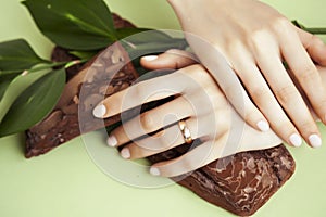 Pretty perfect woman hands with white manicure and green leaf on colorful background with wood, spa cosmetic concept