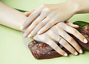 Pretty perfect woman hands with white manicure and green leaf on colorful background with wood, spa cosmetic concept