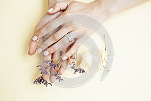Pretty perfect woman hands with white manicure and little flowers on colorful yellow background, spa concept