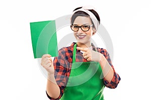 Pretty pin-up girl wearing green apron pointing green cardboard