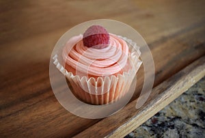 Pretty pink cupcake with icing and red raspberry garnish