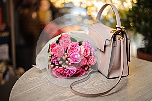 Pretty pink flowers near the stylish handbag on the table