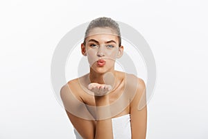 Pretty playful young woman in towel sending a kiss over white background