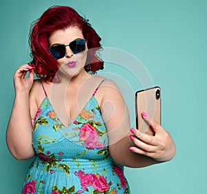 Pretty plus-size fat woman in fashion sunglasses and colorful clothes does fashion sexy selfie on mint photo
